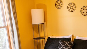 A bedroom with a black bedspread, a bedside table with a lamp, and decorative wall art. - Lakeview Cottage - Myers Cave Resort (North Frontenac)