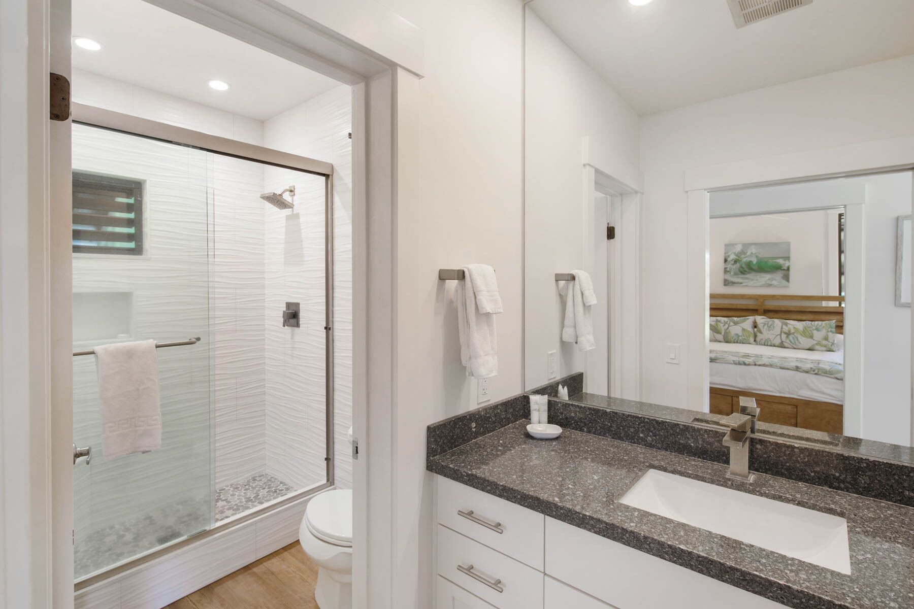 A modern bathroom with a glass-enclosed shower, a white toilet, and a granite countertop with a sink.