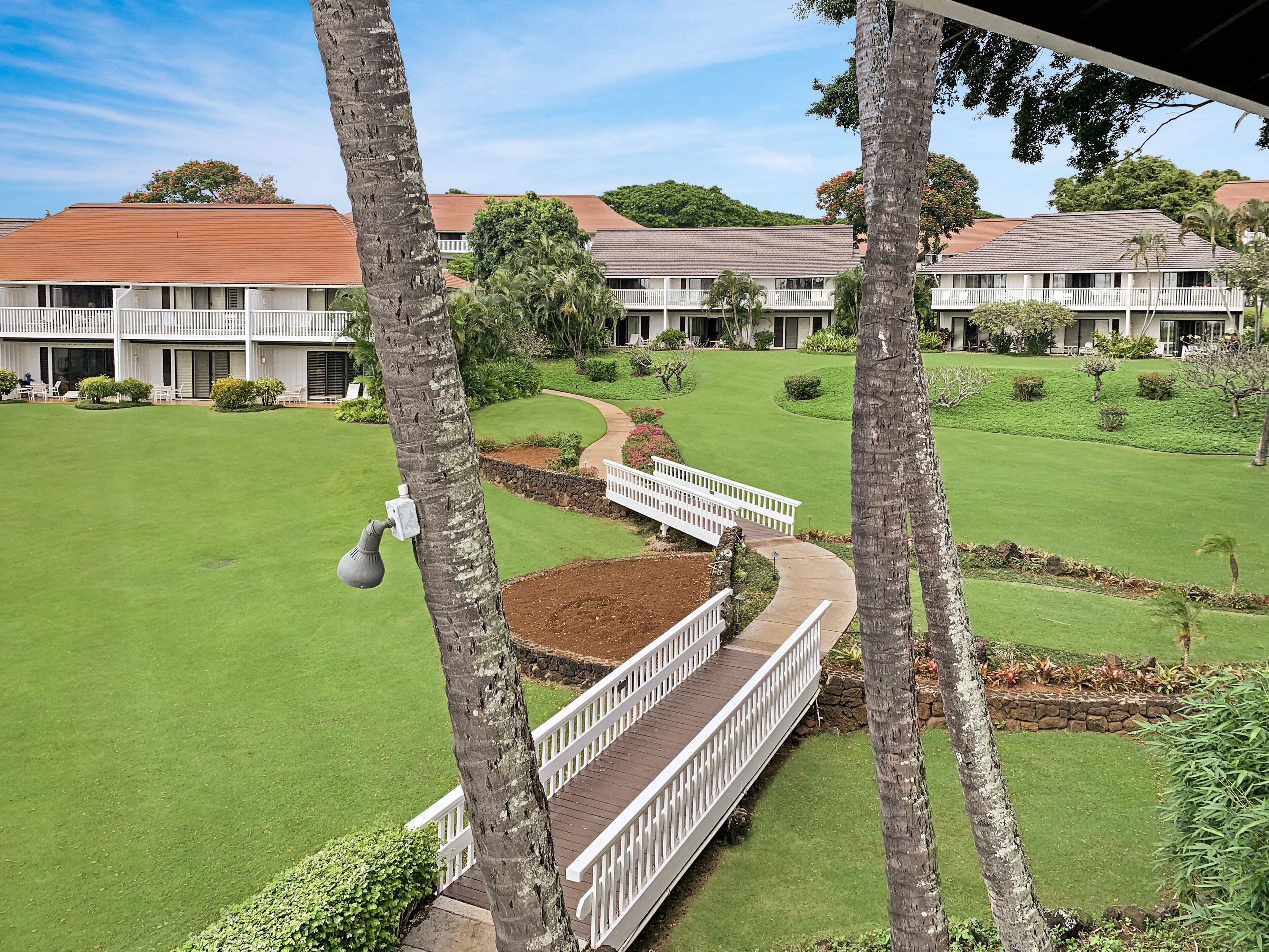 A well-maintained hotel with a lush green lawn, a white bridge, and multiple buildings with red roofs.