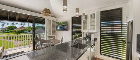 Una cocina moderna con una isla grande, electrodomésticos de acero inoxidable y vistas a un paisaje tropical.