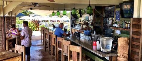 A bar area with wooden chairs and tables, a counter with a water dispenser, and ceiling fans.