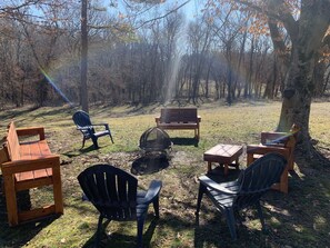 A campsite with wooden benches and chairs arranged around a central fire pit.