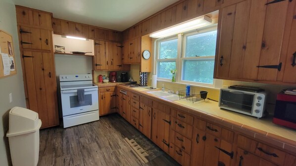 A kitchen with wooden cabinets, a stove, a sink, a toaster, and a clock on the wall.