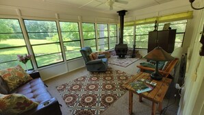 Un solarium con ventanas amplias, una chimenea, un sofá, una butaca y una mesa con una lámpara.