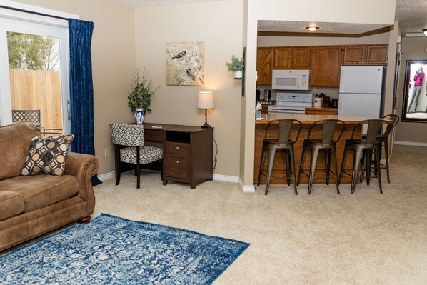 A living room with a brown sofa, a patterned armchair, a desk, and a blue rug.