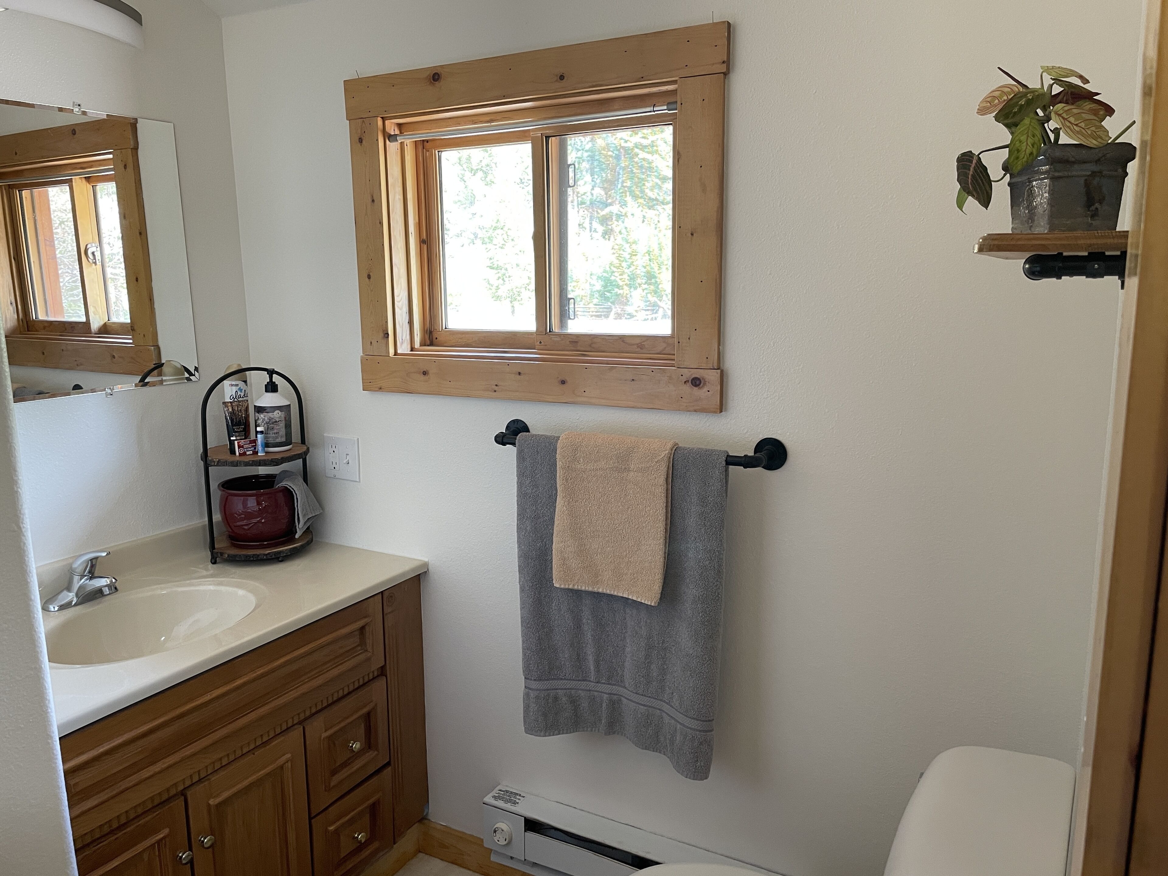 A bathroom with a wooden vanity, a sink, a towel rack, a window, and a small shelf with a plant.