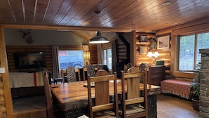 L’intérieur d’un chalet accueillant, avec une table à manger en bois, des chaises, un canapé, une cheminée et un téléviseur.