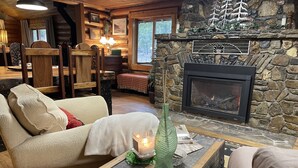 Un salon chaleureux avec une cheminée en pierre, des meubles en bois et une vue sur l’extérieur.