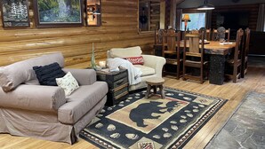 Un intérieur de chalet chaleureux avec un mur en rondins de bois, un canapé, une table à manger avec des chaises et un tapis orné d’un motif d’ours.