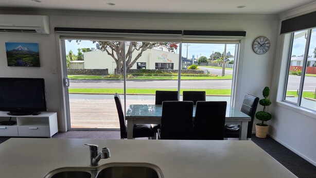 Una cucina moderna con un lavello doppio, zona pranzo con sedie, un tavolino, una televisione su un mobile e un'ampia finestra con vista sulla strada e sul verde.