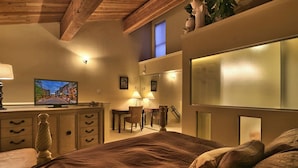 Une chambre à coucher avec un grand lit, un bureau, une chaise et un téléviseur posé sur une commode.