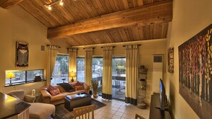 Un salon spacieux avec un plafond en bois, un ensemble de canapés, un téléviseur et un tableau accroché au mur.