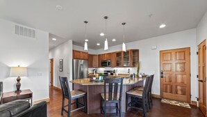 Una cocina moderna con una isla central, armarios de madera, electrodomésticos de acero inoxidable e iluminación colgante.