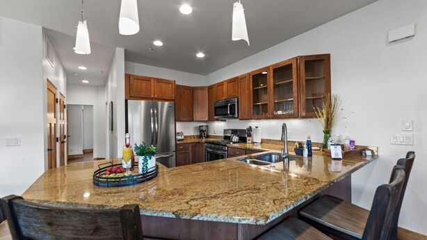 Una cocina moderna con encimeras de granito, electrodomésticos de acero inoxidable, armarios de madera e iluminación colgante.
