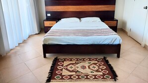 Een slaapkamer met een houten bed, twee nachtkastjes, een kamerkleed met dessin, en twee wandlampen.