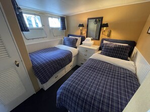 Ein Schlafzimmer mit zwei Betten, einem Schminktisch, einem Spiegel und einem Fenster mit Vorhängen.