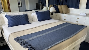 A neatly made bed with a blue blanket and pillows, a bedside table with a lamp, and a dresser with drawers.