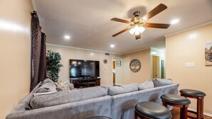 A living room with a sectional sofa, a TV, a ceiling fan, and three bar stools. - Prime Location - Pool Table - BBQ - Walk to AT&T (Arlington)