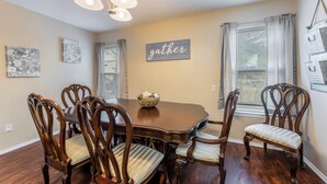A dining room with a wooden table and chairs, a chandelier, and a 'gather' sign on the wall. - Prime Location - Pool Table - BBQ - Walk to AT&T (Arlington)