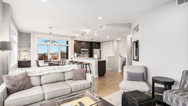 A modern living room with a sofa, armchairs, a coffee table, and a kitchen in the background. - Perfect location! Right downtown! Walking distance to everything. (Grand Haven)