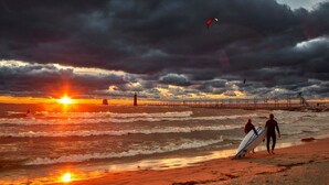 A beach scene with a sunset, waves, and a pier in the background. - Perfect location! Right downtown! Walking distance to everything. (Grand Haven)