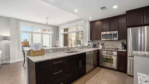 A modern kitchen with dark cabinetry, stainless steel appliances, and a large island with drawers. - Perfect location! Right downtown! Walking distance to everything. (Grand Haven)