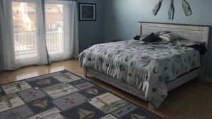 A bedroom with a bed, a window with curtains, a wall-mounted picture, and a wooden floor. - Best location on the island (Brigantine)