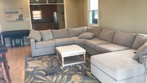 A living room with a sectional sofa, a coffee table, and a rug. There is a kitchen in the background. - Best location on the island (Brigantine)