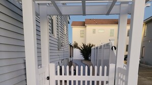 En grindad entré med ett vitt staket, en asfalterad gångväg och en liten trädgårdsyta med en krukväxt.