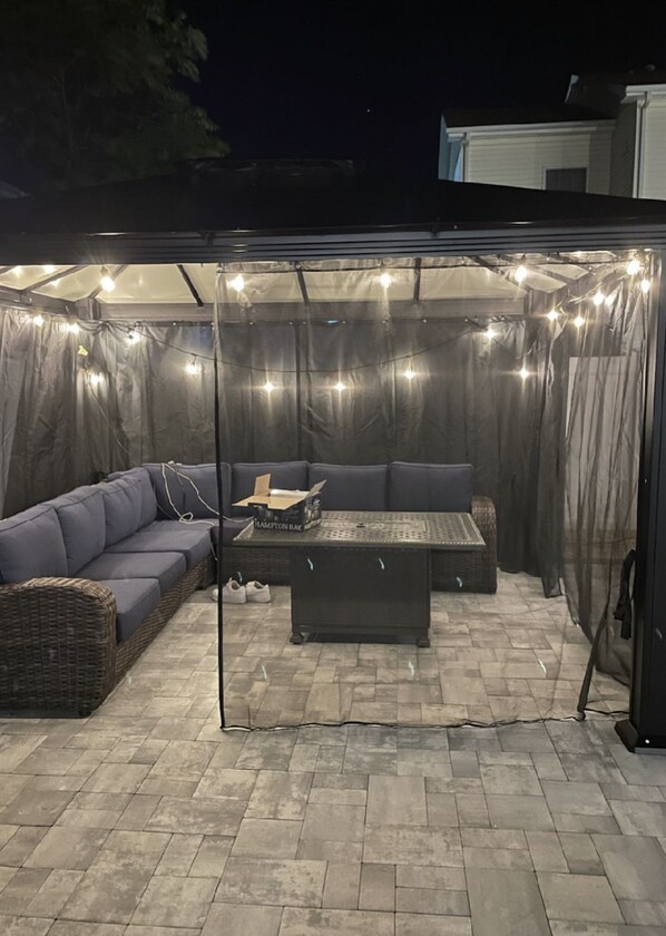Een terras buiten met een overdekte zithoek, een tafel en sfeerverlichting.
