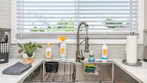 A kitchen with a stainless steel sink, a dish rack, a potted plant, and various cleaning supplies. - Parkside Estate, Niagara Falls, USA + Free Parking (Niagara Falls)