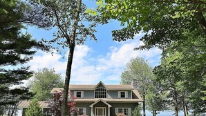 Une maison à deux étages, dotée d’un toit à pignon, d’un porche à l’avant et d’une cheminée en pierre.