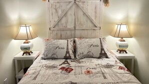Una cama con edredón con motivos de París, dos lámparas de noche y un cabecero de madera rústica.