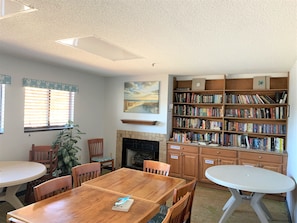 A cozy library with a fireplace, wooden bookshelves, and a dining area with chairs and tables.