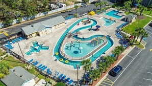 Un área de piscina con varias piscinas, sillones de descanso y un pequeño edificio.
