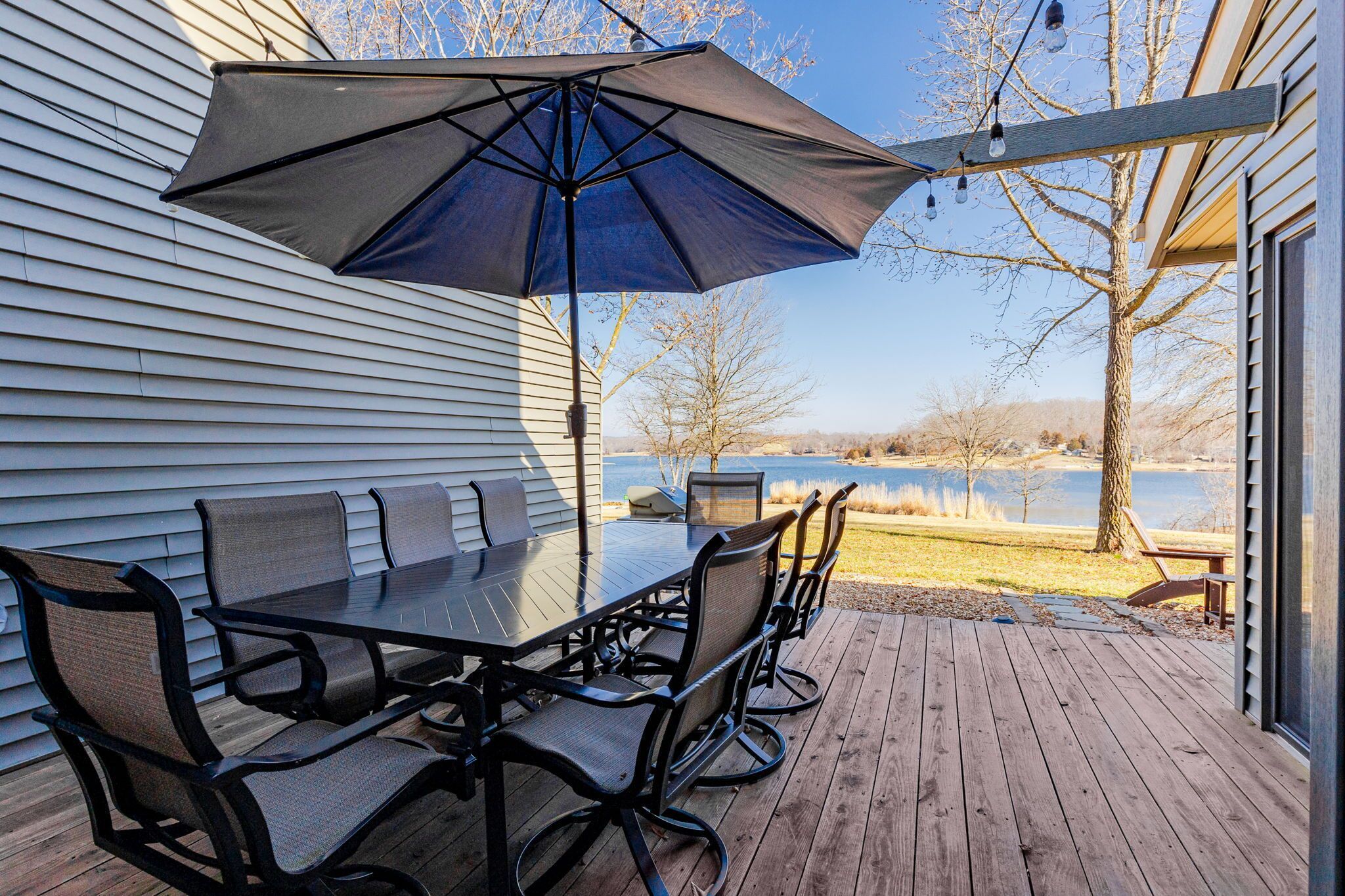 Une terrasse avec une table et des chaises, un grand parasol et une vue sur un lac.