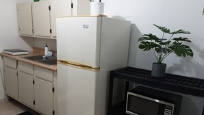 Une cuisine de taille réduite avec un réfrigérateur blanc, un four à micro-ondes posé sur un meuble noir et une plante en pot sur le plan de travail.