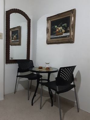 Intimate dining area with a round table and two chairs, accompanied by a still life painting and a decorative mirror.