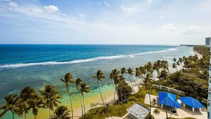 Blick auf einen Strand mit Palmen, einem klaren Himmel und einem Gebäude mit blauen Dächern.