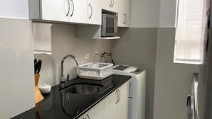 A modern kitchen with white cabinets, a black countertop, a built-in microwave, a sink, and a dishwasher. - Bright 2BR Apartment Steps from El Olivar Park (San Isidro)