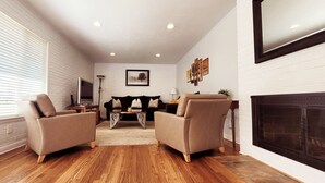 Un salon moderne avec deux fauteuils beiges, un canapé noir, une table basse en bois et une cheminée.