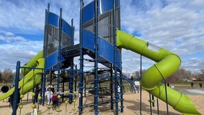 Une aire de jeux avec une structure d’escalade bleue et verte et des toboggans.