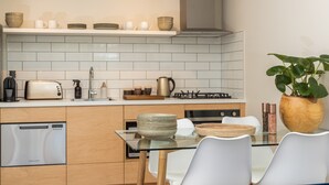 Een moderne keuken met een vaatwasser, fornuis en een eettafel met glazen blad en stoelen.