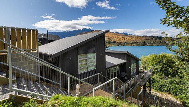 Een modern huis met een terras met uitzicht op een meer en bergen.