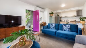 Een moderne woonkamer met een blauwe bank, een televisie en een keuken op de achtergrond.