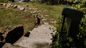 Ein Betonweg führt zu einer Bank an einem See, umgeben von Bäumen und Felsen.
