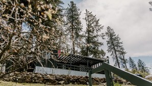 Eine rustikale Holzhütte mit einer Holzterrasse, umgeben von hohen Kiefern und einer Steinmauer.