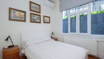 Ein Schlafzimmer mit einem Bett, einem Nachttisch, einer Lampe, einem Fenster und drei gerahmten Bildern an der Wand.