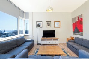 Una sala de estar moderna con un gran ventanal, un televisor de pantalla plana y un conjunto de sofás.