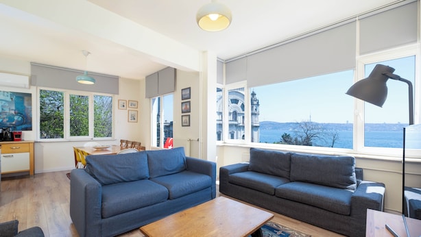 A modern living room with two sofas, a coffee table, and large windows offering a view of the city.